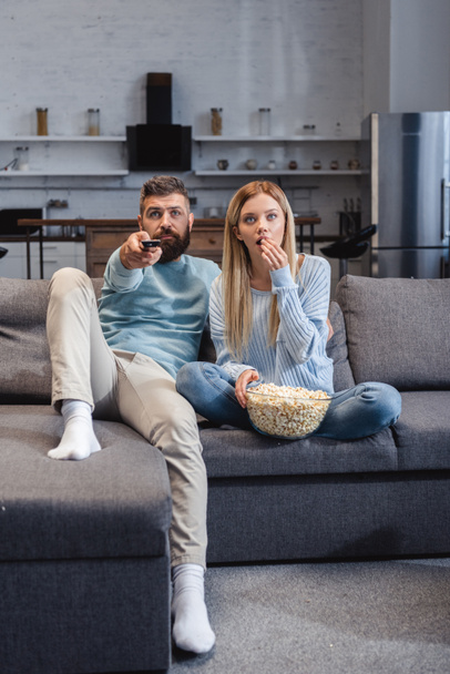 Couple sitting on sofa with popcorn and watching movie  - Photo, Image