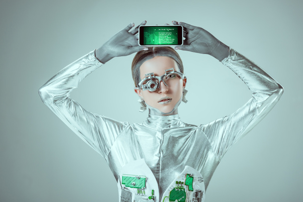 srebrny robot trzyma smartphone z urządzenia nad głową na białym tle na koncepcji technologii przyszłości, szary - Zdjęcie, obraz