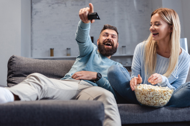 Husband and wife laughing and sitting on sofa with popcorn  - Φωτογραφία, εικόνα