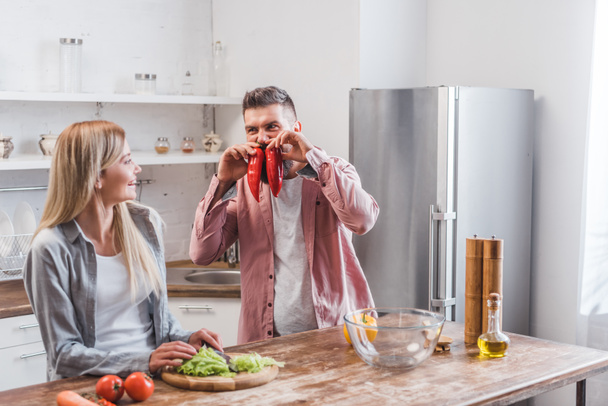 Cheerful husband playing with vegetables near wife - Photo, Image