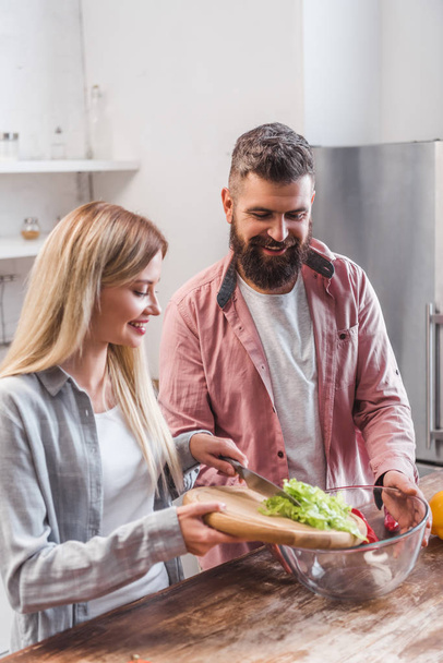 Couple debout dans la cuisine et ajouter des feuilles de salade dans le bol
  - Photo, image