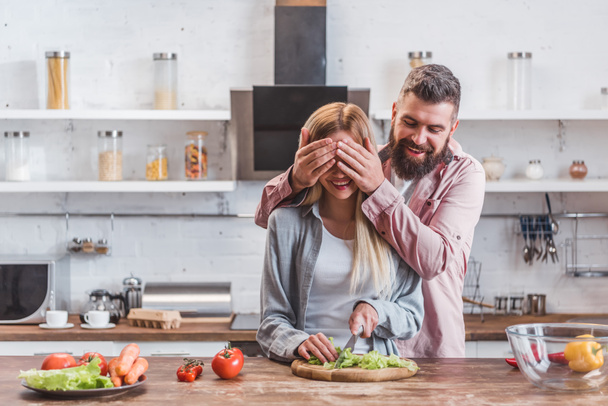 Husband smiling and closing eyes of wife in kitchen  - Photo, Image