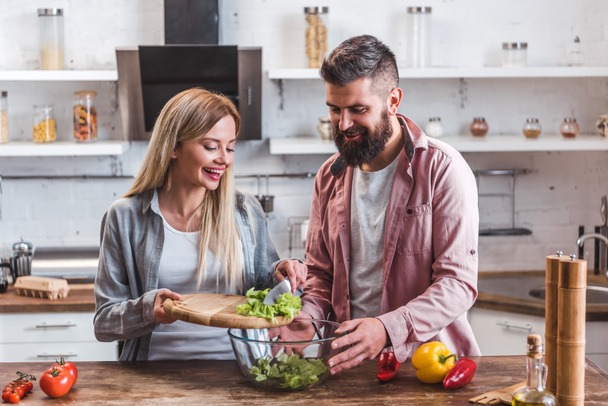 Couple joyeux ajoutant des feuilles de salade dans un bol
  - Photo, image