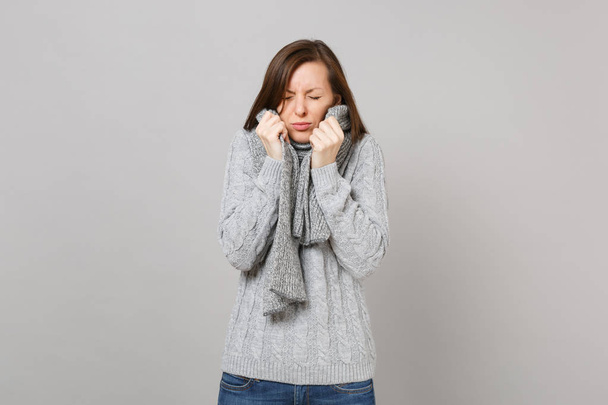 灰色の背景のスタジオ ポートレートに分離されたスカーフ維持目を閉じての灰色のセーター ラッピングの病気の少女。ライフ スタイル健康病気病気病気治療寒い季節概念。コピー スペースをモックアップします。 - 写真・画像
