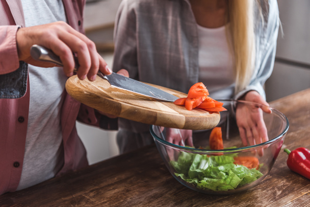 Cropped view of man adding tomatoes in salad and woman holding bowl  - Foto, afbeelding