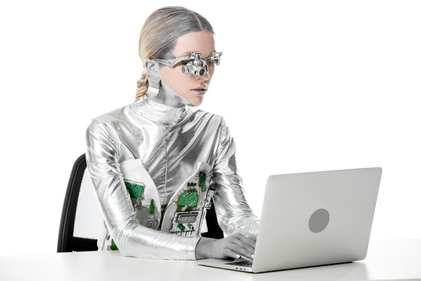 robot d'argento seduto a tavola e lavorare con il computer portatile isolato su bianco, concetto di tecnologia futura
 - Foto, immagini