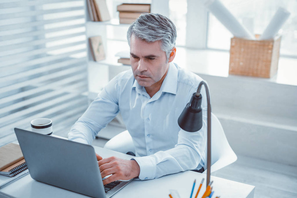 Hombre serio de pelo gris sentado en su lugar de trabajo
 - Foto, imagen