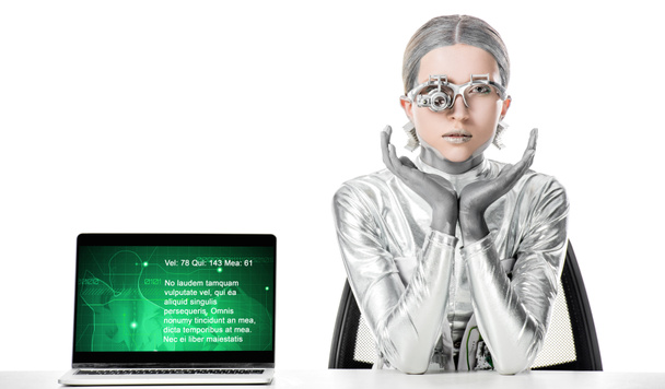 robot d'argento seduto a tavola vicino al computer portatile con elettrodomestico medico isolato su bianco, concetto di tecnologia futura
 - Foto, immagini