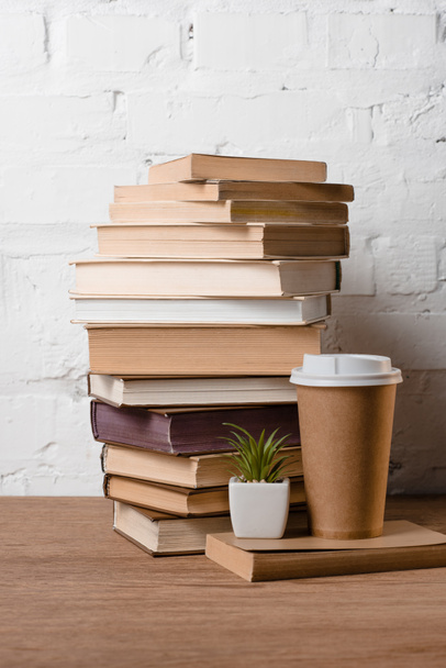 hromadu knih, zelené v květináči a káva s sebou na dřevěný stůl - Fotografie, Obrázek