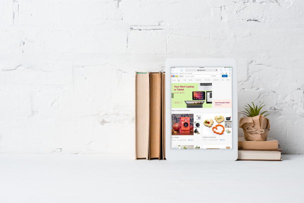 ψηφιακή δισκίο με ebay εφαρμογή, βιβλία και πράσινο σε δοχείο εγκαταστάσεις κοντά σε λευκό τοίχο - Φωτογραφία, εικόνα