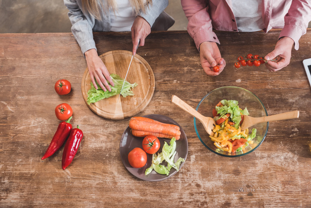 cropped view of couple cooking vegetable salad together at wooden table - Foto, Imagem