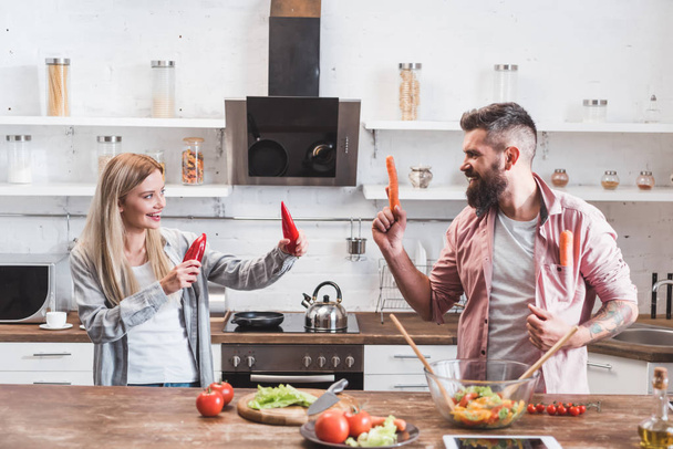 funny couple playing with vegetables while cooking dinner at wooden table - Photo, Image