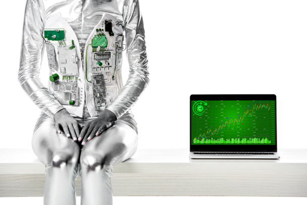 cropped image of robot sitting on table near laptop with chart appliance isolated on white, future technology concept - Foto, Bild