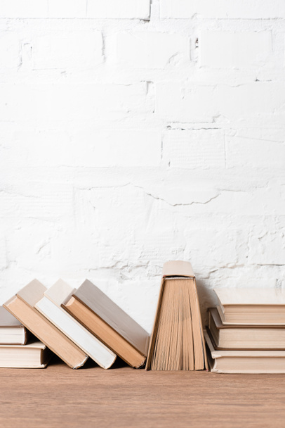 books with hardcovers on wooden table near white brick wall   - Photo, Image