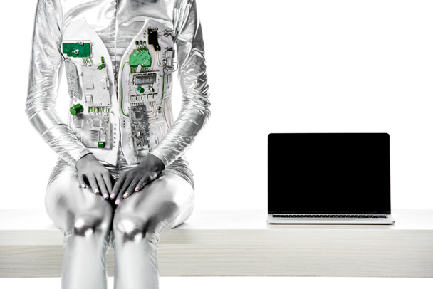 immagine ritagliata di robot seduto sul tavolo vicino al computer portatile con schermo bianco isolato su bianco, concetto di tecnologia futura
 - Foto, immagini