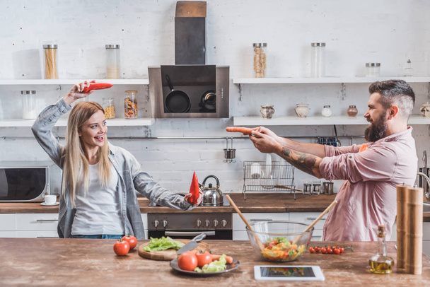 divertente coppia che gioca con le verdure mentre cucina la cena in cucina
 - Foto, immagini