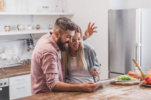 χαρούμενο ζευγάρι χρησιμοποιώντας ψηφιακό tablet και χειρονομίες στην κουζίνα - Φωτογραφία, εικόνα