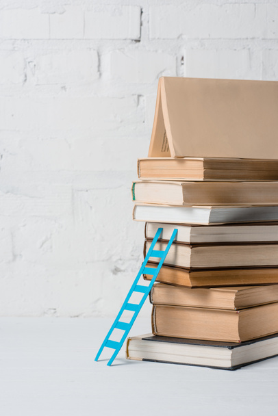 pile of books and small blue step ladder near white brick wall - Фото, изображение