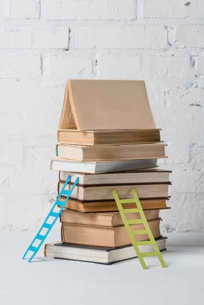 σωρός από βιβλία και μικρό βήμα σκάλες κοντά σε λευκό τοίχο - Φωτογραφία, εικόνα