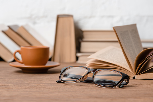 close-up view of eyeglasses, cup of coffee and books on wooden table - Fotografie, Obrázek