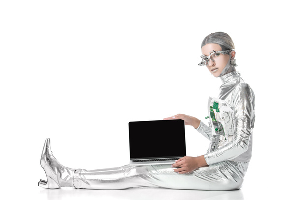 robot plateado sentado y mostrando portátil con pantalla en blanco aislado en blanco, concepto de tecnología futura
 - Foto, imagen
