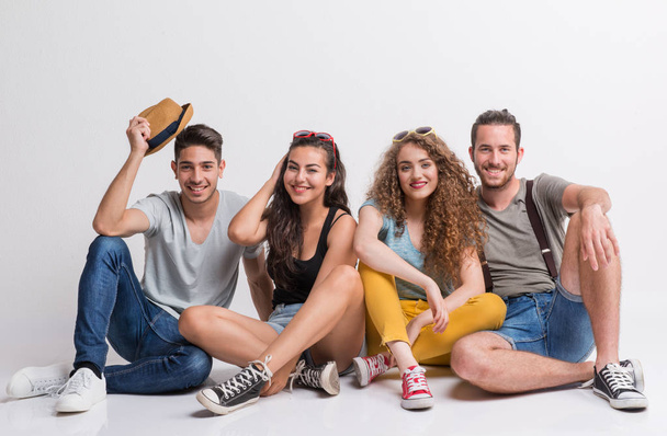 Portrait of joyful young group of friends sitting on the ground in a studio, having good time. - Photo, Image