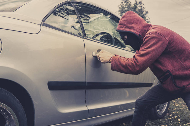 Side view of car being forced by a man in hoodie and mask. Thief tries to steal vehicle from a parking. Young male acts alone breaking the car door. Unknown person picklocks the automobile. Car fraud - Photo, Image