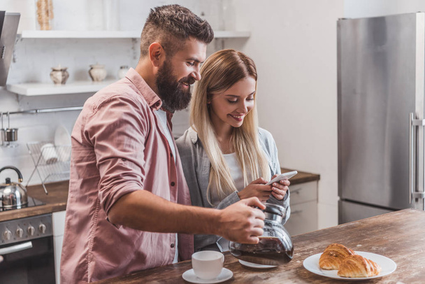 cheerful couple having breakfast and using smartphone at kitchen - Фото, зображення