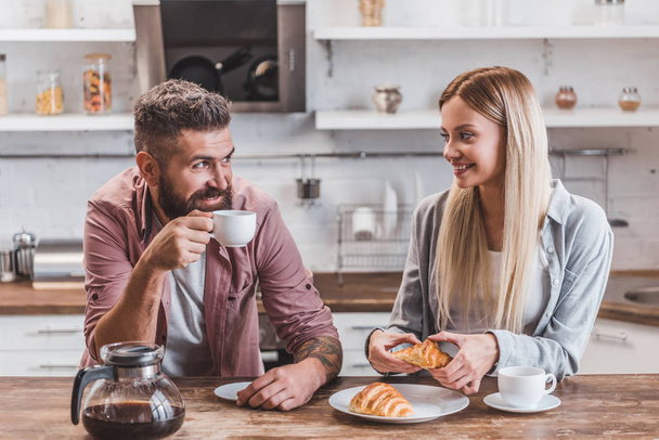 young cheerful couple eating croissants and drinking coffee for breakfast - Foto, Bild