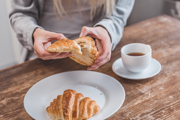 vista cortada de mãos femininas segurando croissant na mesa de madeira
 - Foto, Imagem
