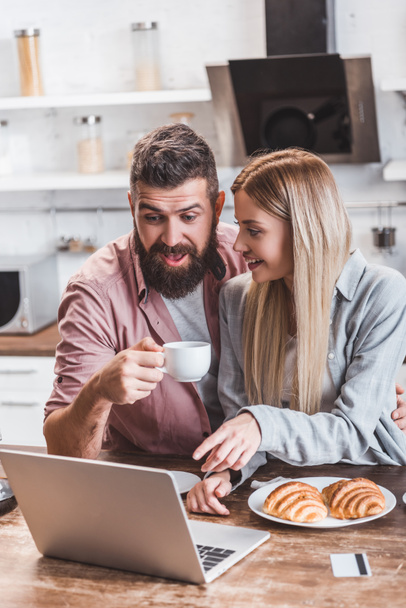 attractive woman pointing at laptop screen while happy man drinking coffee - Foto, Imagem