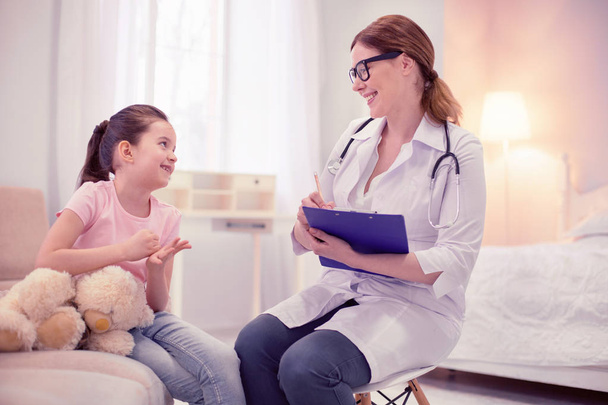 Cute dark-haired girl sitting near her toy looking at general practitioner - Фото, зображення