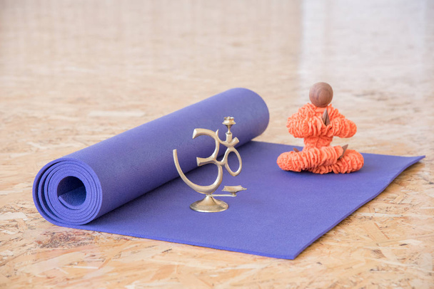 Figur in orangefarbener Kleidung sitzt in einer Yoga-Pose mit einer lila Matte für Bewegung und Meditation - Foto, Bild