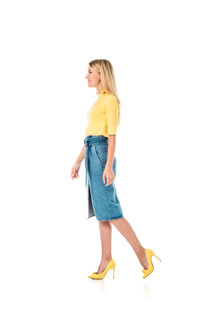 side view of attractive woman in yellow shirt and denim skirt walking isolated on white - Fotoğraf, Görsel