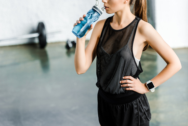 Ausgeschnittener Blick auf fitte Sportlerin, die im Fitnessstudio Wasser aus Sportflasche trinkt - Foto, Bild