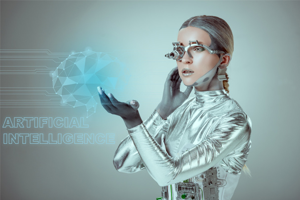 futuristic silver cyborg touching digital data with "artificial intelligence" lettering isolated on grey, future technology concept   - Photo, Image