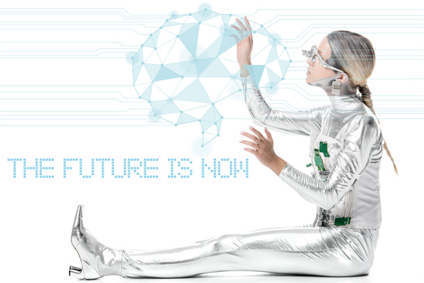 side view of silver cyborg sitting and touching digital data isolated on white with "the future is now" lettering - Photo, Image