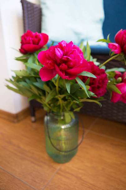 un bouquet de beaux pions dans un grand vase se dresse sur le sol près du canapé avec des oreillers
 - Photo, image