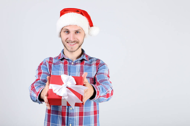 Young man in santa hat holding gift box on grey background - Foto, imagen