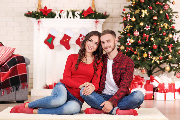 Happy young couple sitting at home near christmas tree - Fotoğraf, Görsel