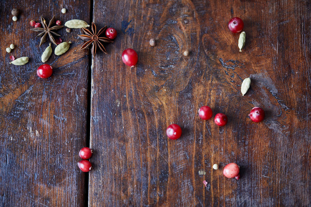 top view of scattered cranberries, carnation and pepper on wooden table in kitchen - Foto, Bild