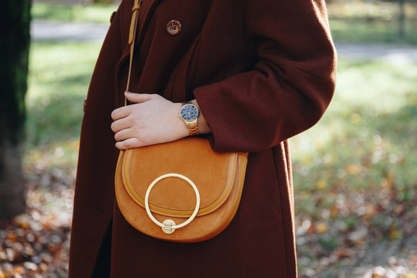 pouliční styl módní detaily. zblízka, mladý módní blogger nosí hnědý zimní kabát a černé a zlaté Náramkové hodinky. Kontrola času, drží krásné semišové kožené peněženky. - Fotografie, Obrázek