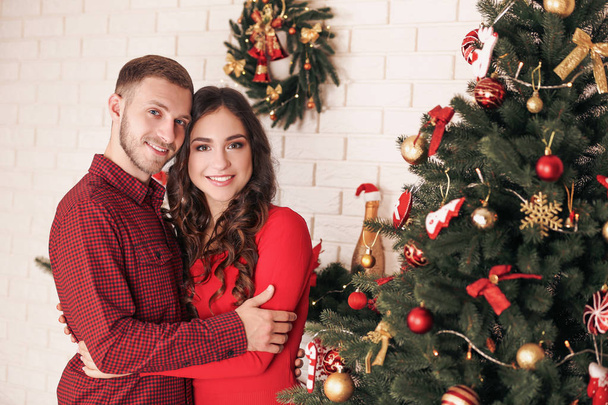 Happy young couple standing at home near christmas tree - Valokuva, kuva
