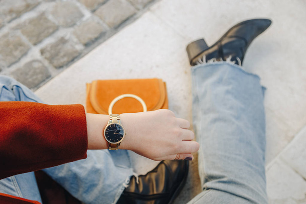 street style fashion details. close up, young fashion blogger wearing brown winter coat, and a black and golden analog wrist watch. checking the time, holding a beautiful suede leather purse. - Φωτογραφία, εικόνα