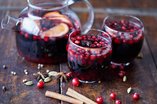 homemade mulled wine with cranberries in glasses and teapot on wooden table in kitchen - Фото, зображення