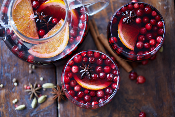 elevated view of homemade mulled wine with cranberries, cinnamon sticks and oranges on tabletop in kitchen - Fotografie, Obrázek