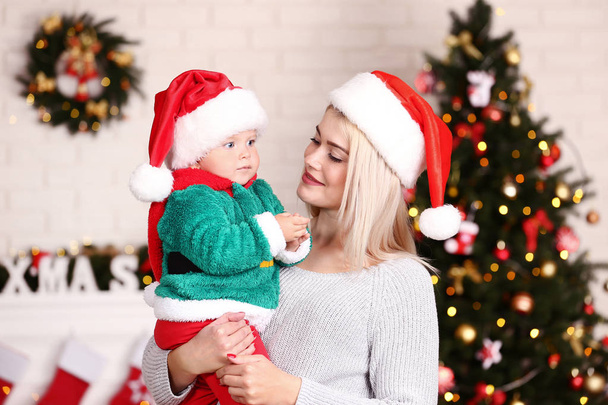 Mother and baby boy in santa hats celebrating christmas at home - 写真・画像