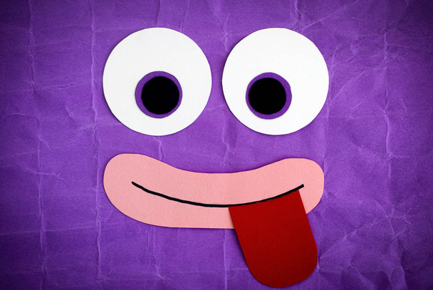 Funny face with tongue stuck out. Emotional face made from paper. Purple background. - Fotografie, Obrázek