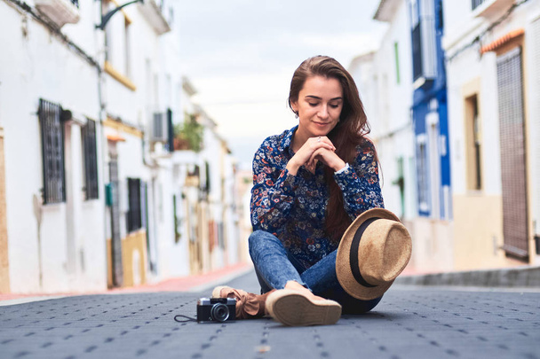 Jonge lachende vrouw, die zit op weg met kleine kleurrijke gebouwen in de Spaanse stad Denia. - Foto, afbeelding