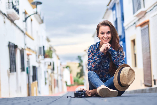 Fiatal mosolygó nő ül a kis színes épületek a spanyol városban Denia úton. - Fotó, kép